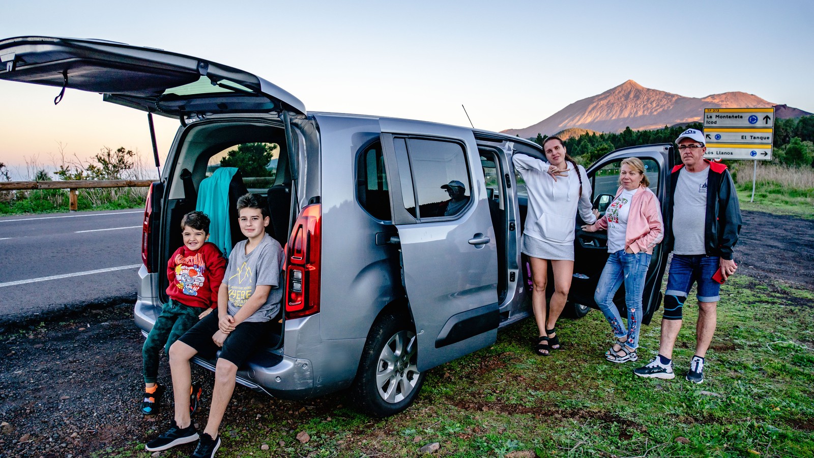 Family standing beside a passenger van during a road trip, illustrative