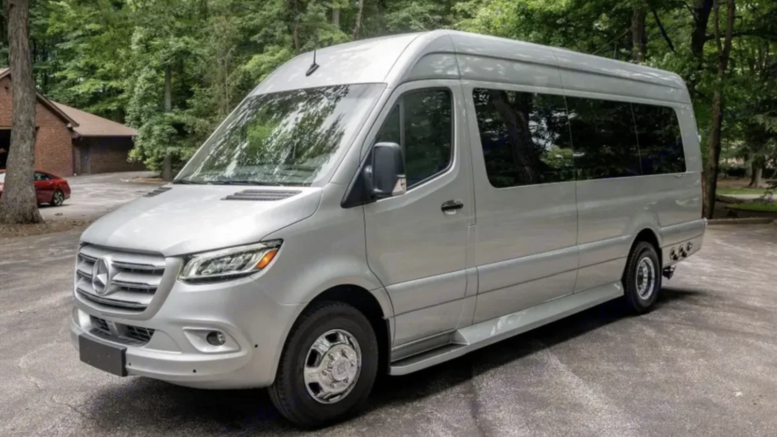 Front three-quarter view of the actual silver 2023 Mercedes-Benz luxury passenger van listed by Dufourfun Vans, parked beside trees.