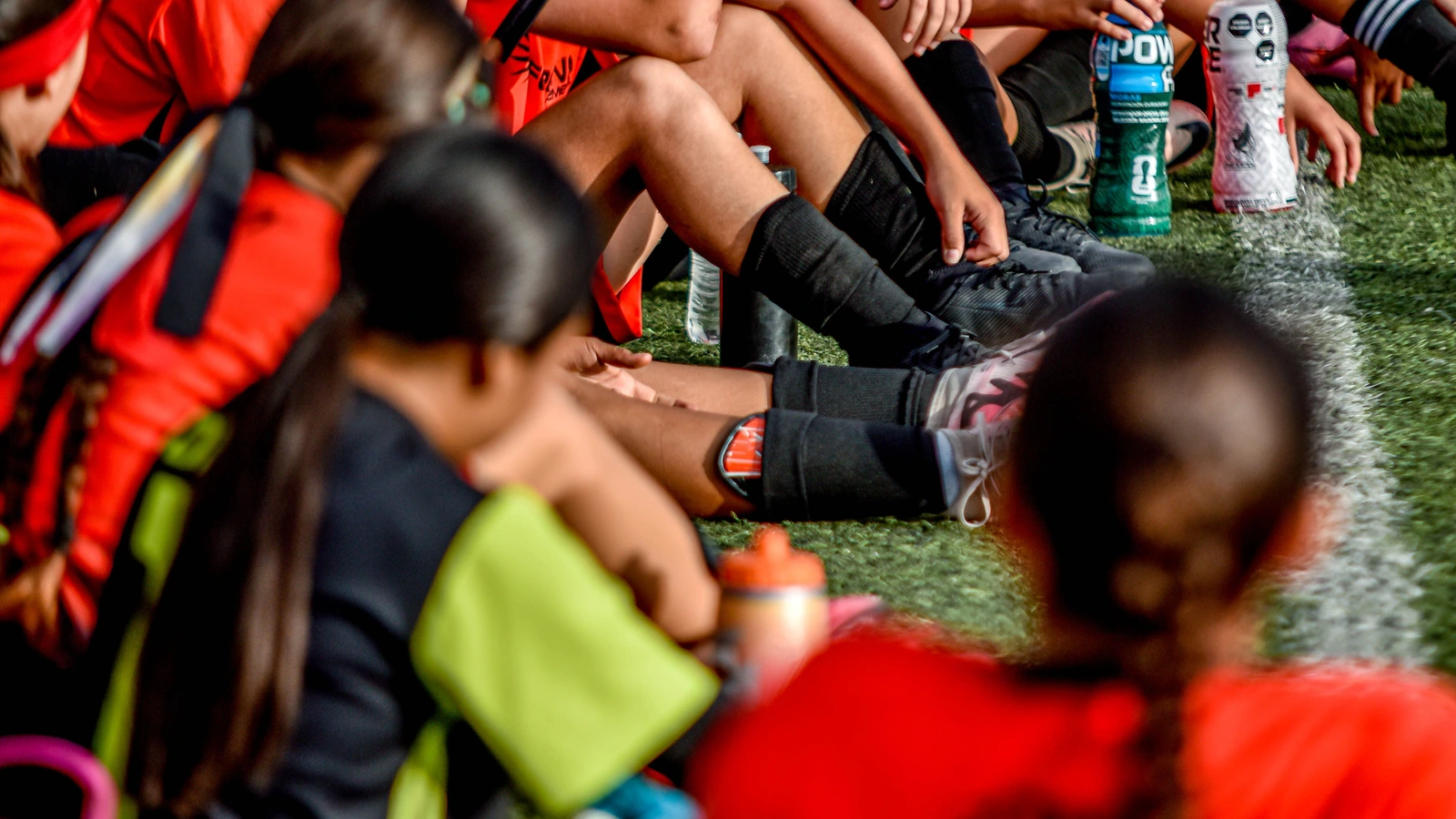 Young soccer players resting together on the sidelines with water bottles; illustrative team photo.